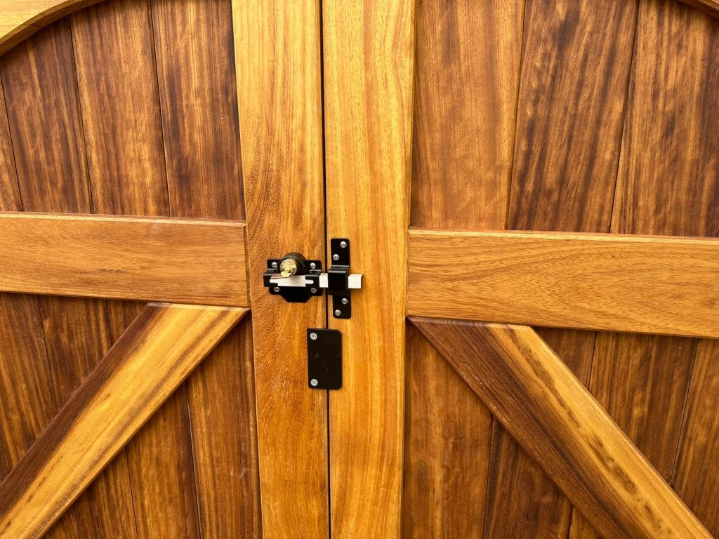 Close-up of bespoke iroko driveway gates showing the centre meeting stile, black ironmongery handle, and drop bolt detail.