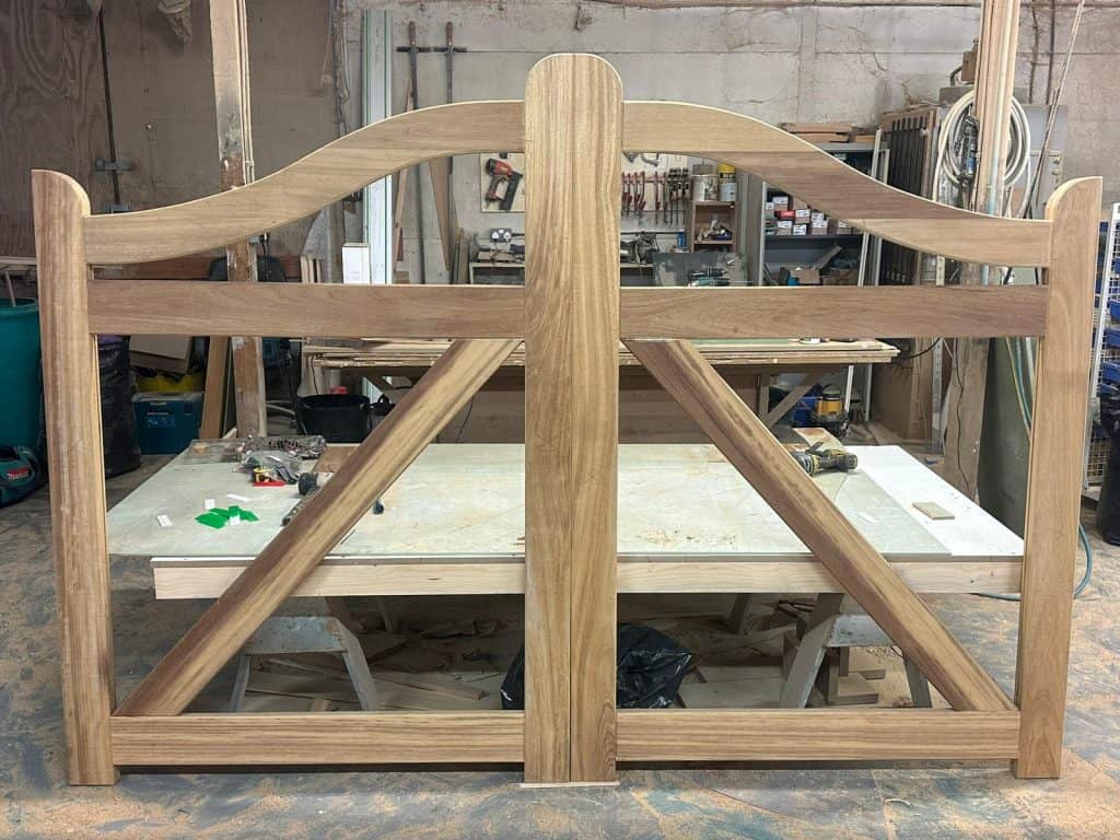 Rear view of bespoke iroko driveway gate frames in the workshop, showing traditional bracing and curved top rail before panel installation.