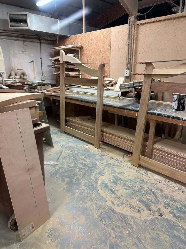 Handcrafted iroko driveway gates in the workshop during frame assembly, showing curved top rail clamped in position.