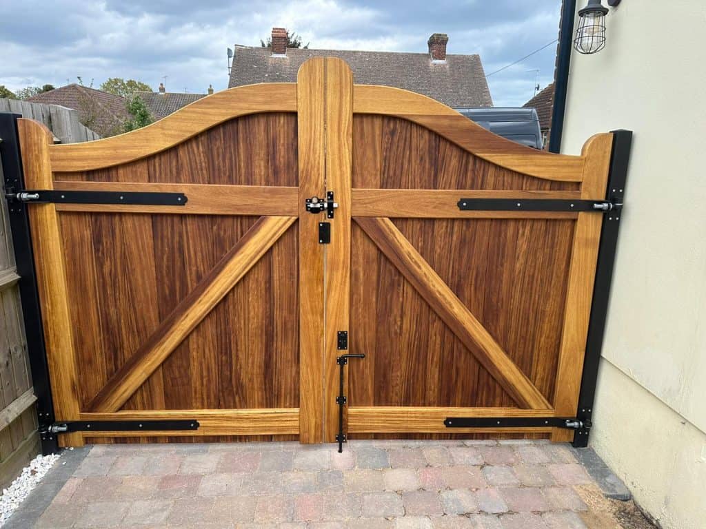 Bespoke iroko driveway gates installed at a private driveway in Wickham Bishops, Essex, featuring a curved top profile and solid hardwood panels.