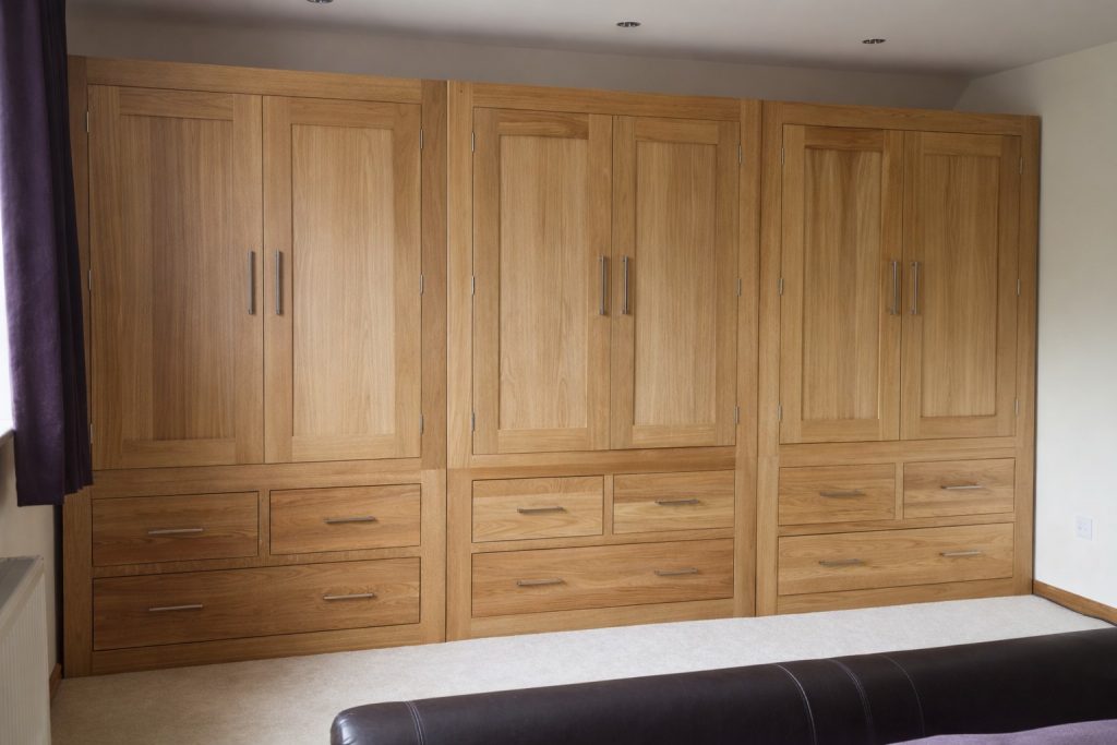Bespoke oak fitted wardrobes with integrated drawers and panelled doors, handcrafted and installed in a bedroom in Essex