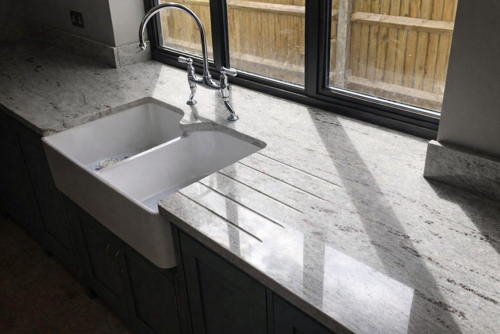 Close-up of a bespoke Green Smoke shaker kitchen featuring a farmhouse sink, quartz worktops, and traditional chrome bridge tap in Chorleywo