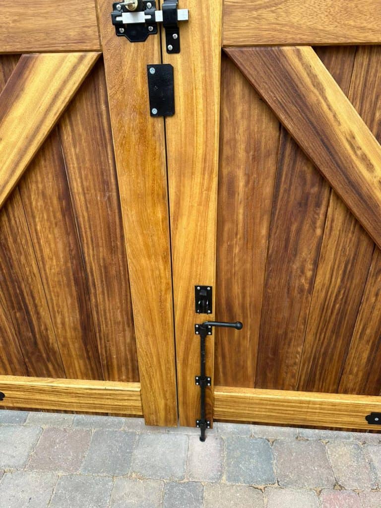 Detail of bespoke iroko driveway gate centre joint with black external-grade ironmongery and traditional bracing visible.