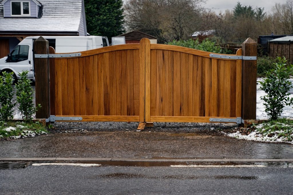 Bespoke Iroko timber driveway gates with an arched top and solid vertical boards, professionally installed at a home in Great Saling, Essex