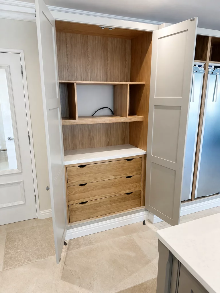 Grey in-frame kitchen installation with oak interiors and white quartz worktops in Braintree, open tall cabinet revealing oak-lined drawers and shelving.