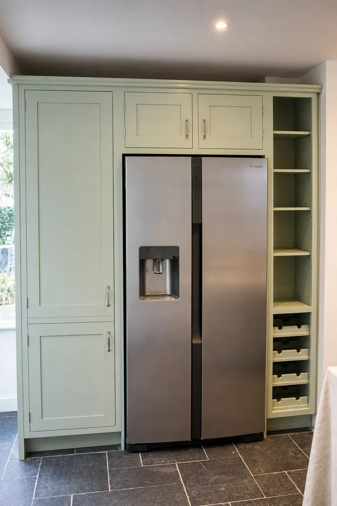 Cooking Apple Green Shaker kitchen with oak worktops and a tiled range recess, tall fridge-freezer housing with integrated wine storage.