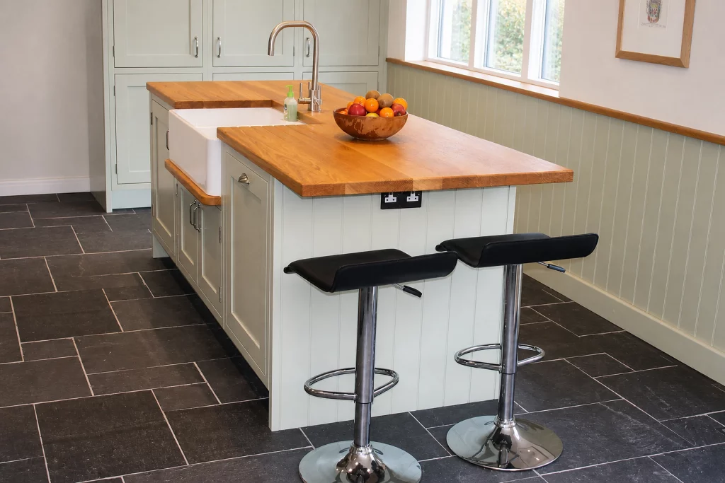 Cooking Apple Green Shaker kitchen with oak worktops and a tiled range recess, oak-topped island with sink and two stools.