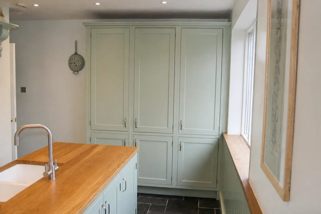 Cooking Apple Green Shaker kitchen with oak worktops and a tiled range recess, island foreground with full-height cupboards beyond.