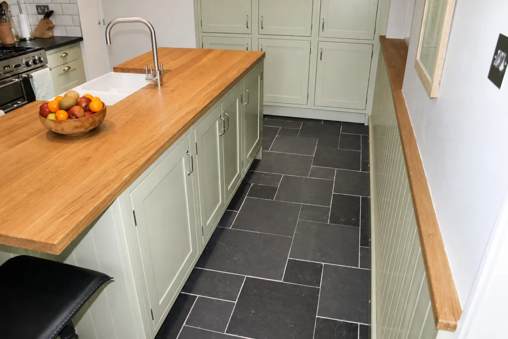 Cooking Apple Green Shaker kitchen with oak worktops and a tiled range recess, long perspective along the oak-topped island.