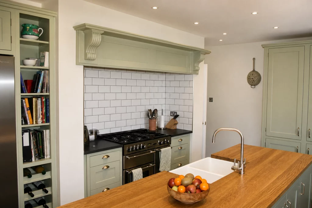 Cooking Apple Green Shaker kitchen with oak worktops and a tiled range recess, wide view from the island towards the range recess.