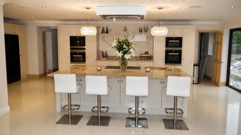 Dimpse-painted Shaker kitchen with a large granite island and integrated appliances, symmetrical wide view of the island and rear cabinetry.