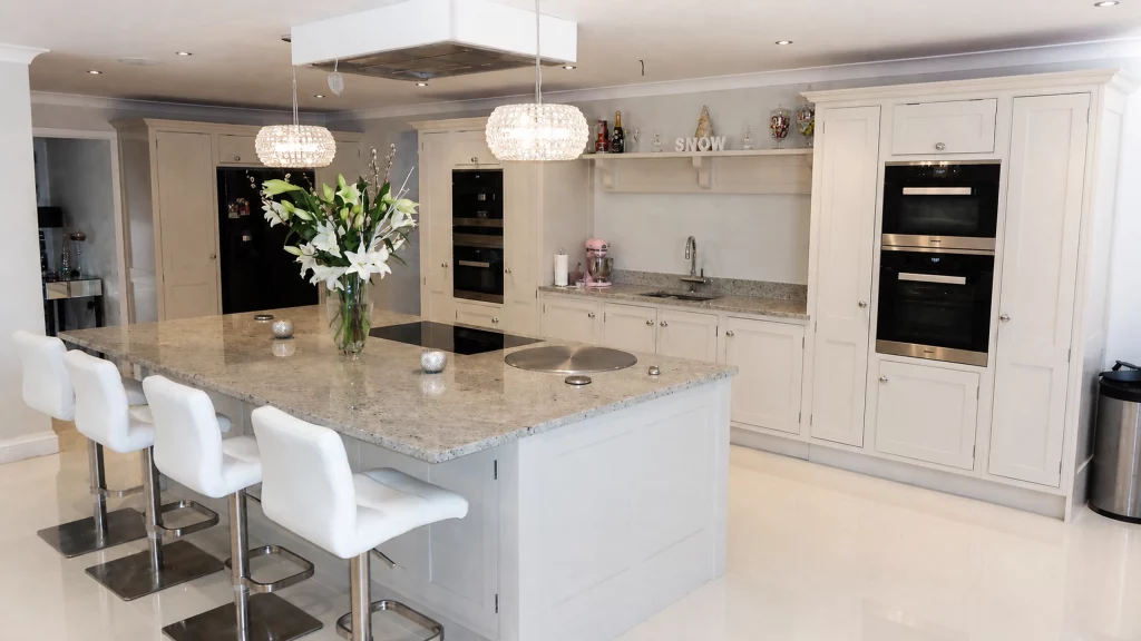 Dimpse-painted Shaker kitchen with a large granite island and integrated appliances, wide island view with four white bar stools.
