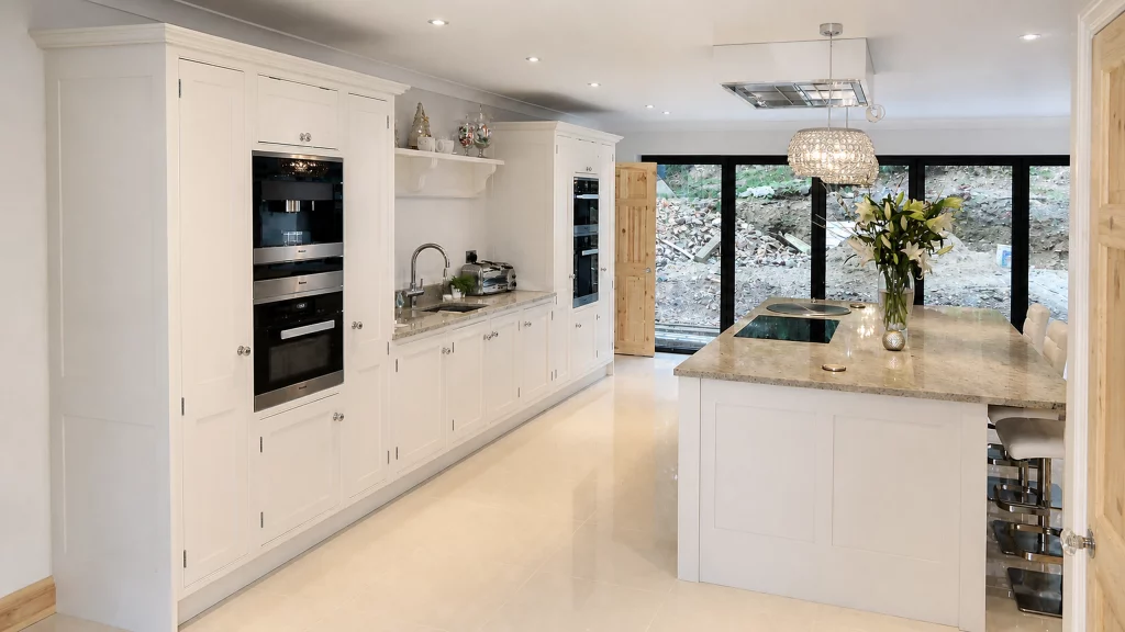 Dimpse-painted Shaker kitchen with a large granite island and integrated appliances, long view down the fitted cabinet run.