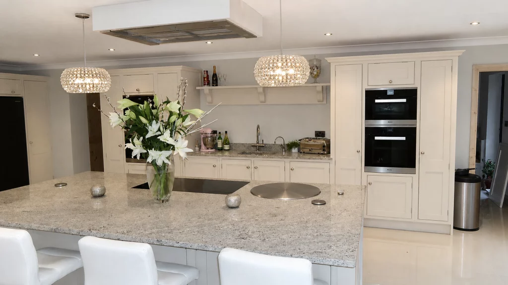 Dimpse-painted Shaker kitchen with a large granite island and integrated appliances, close view across the granite island towards the sink run.