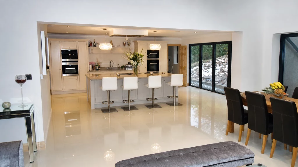Dimpse-painted Shaker kitchen with a large granite island and integrated appliances, kitchen seen through the wide opening from the dining space.