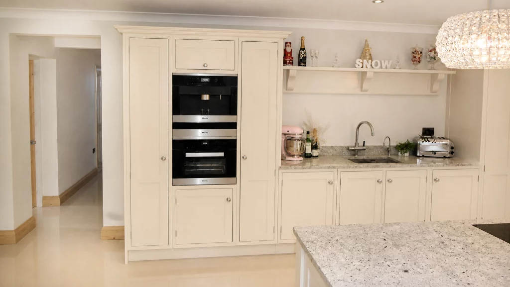 Dimpse-painted Shaker kitchen with a large granite island and integrated appliances, tall oven housing and sink run detail.