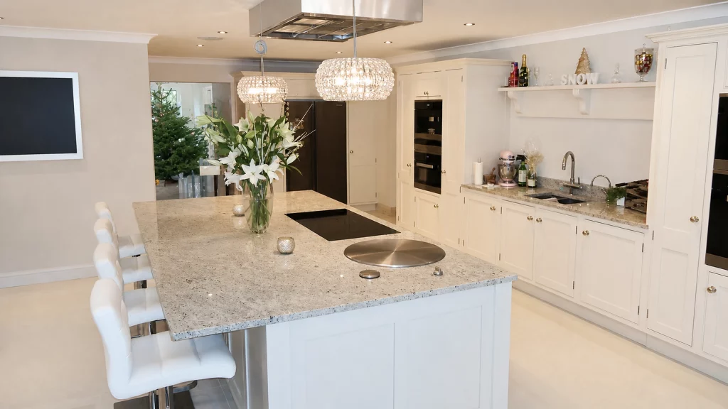 Dimpse-painted Shaker kitchen with a large granite island and integrated appliances, island and rear cabinetry viewed from the side.