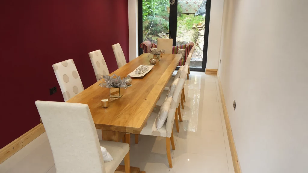 Dimpse-painted Shaker kitchen with a large granite island and integrated appliances, oak dining table set against a deep red feature wall.
