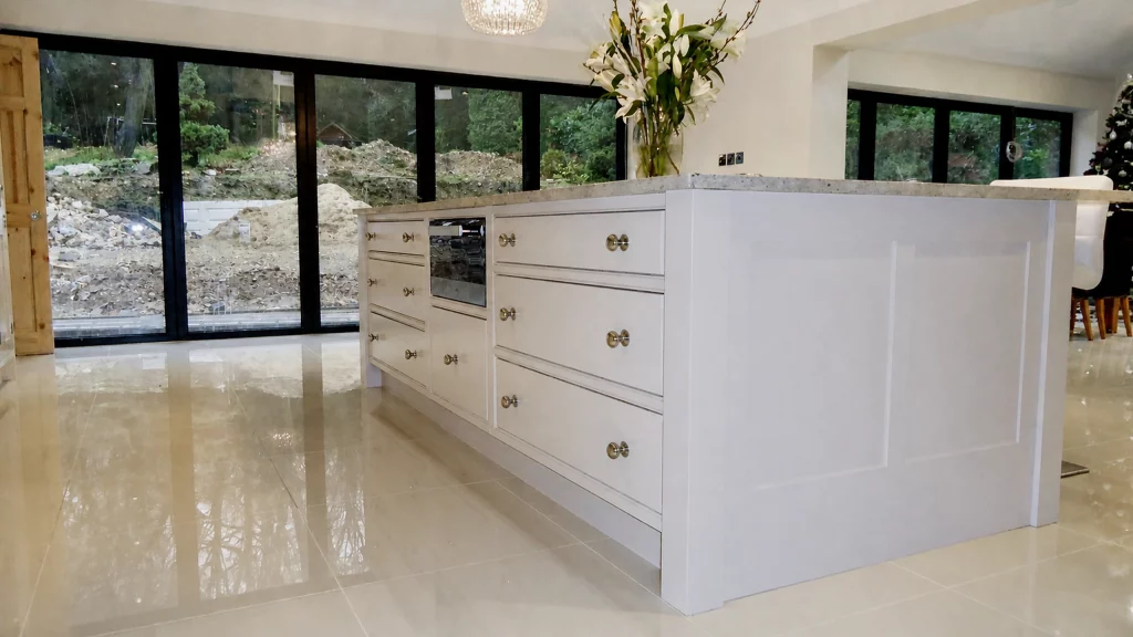 Dimpse-painted Shaker kitchen with a large granite island and integrated appliances, rear view of the island showing drawer storage.