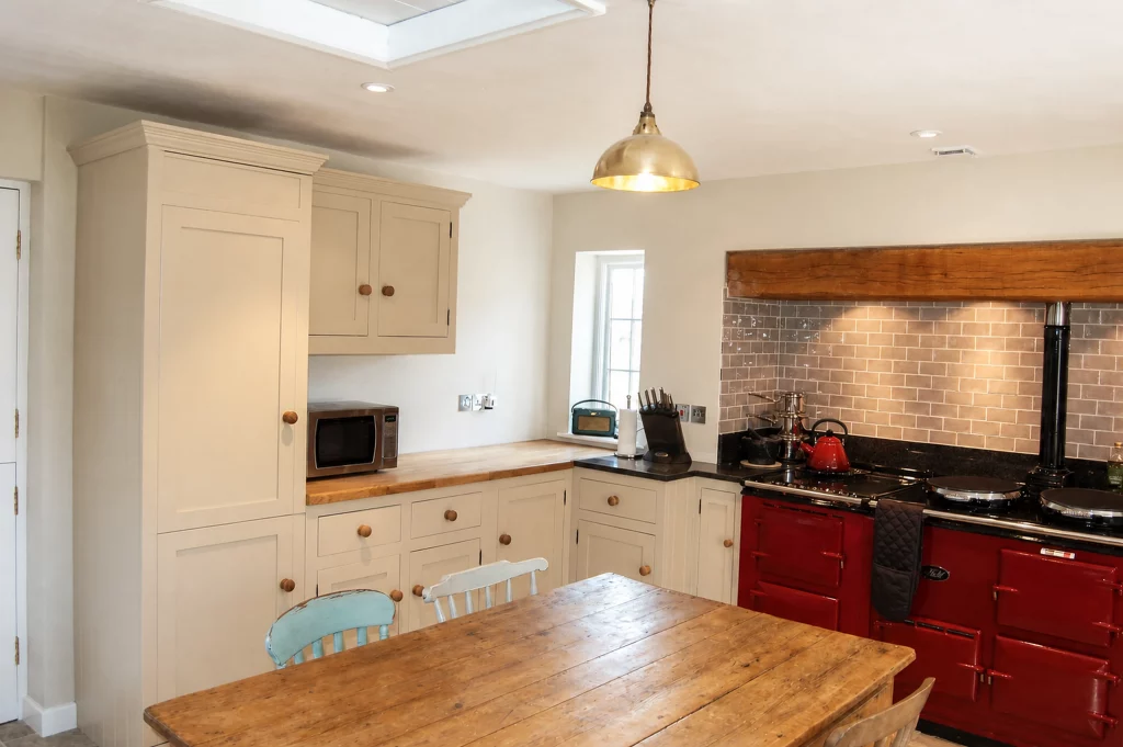 Painted Shaker kitchen with a red AGA, granite and oak worktops, wide view from the dining table towards the AGA and larder.