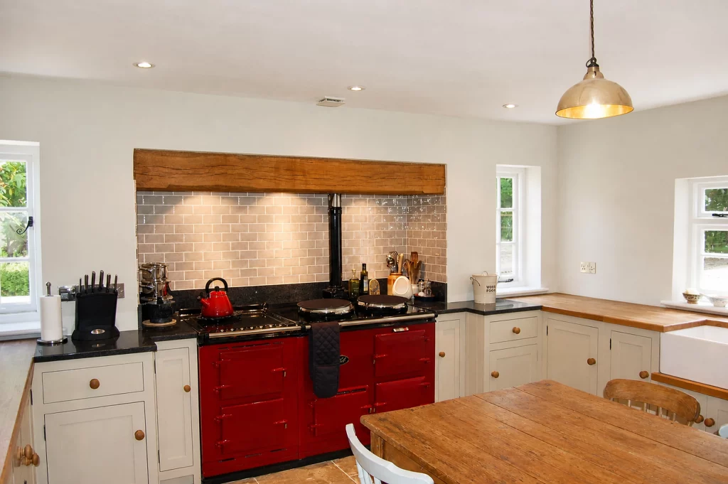 Painted Shaker kitchen with a red AGA, granite and oak worktops, front view of the red AGA within the tiled cooking recess.