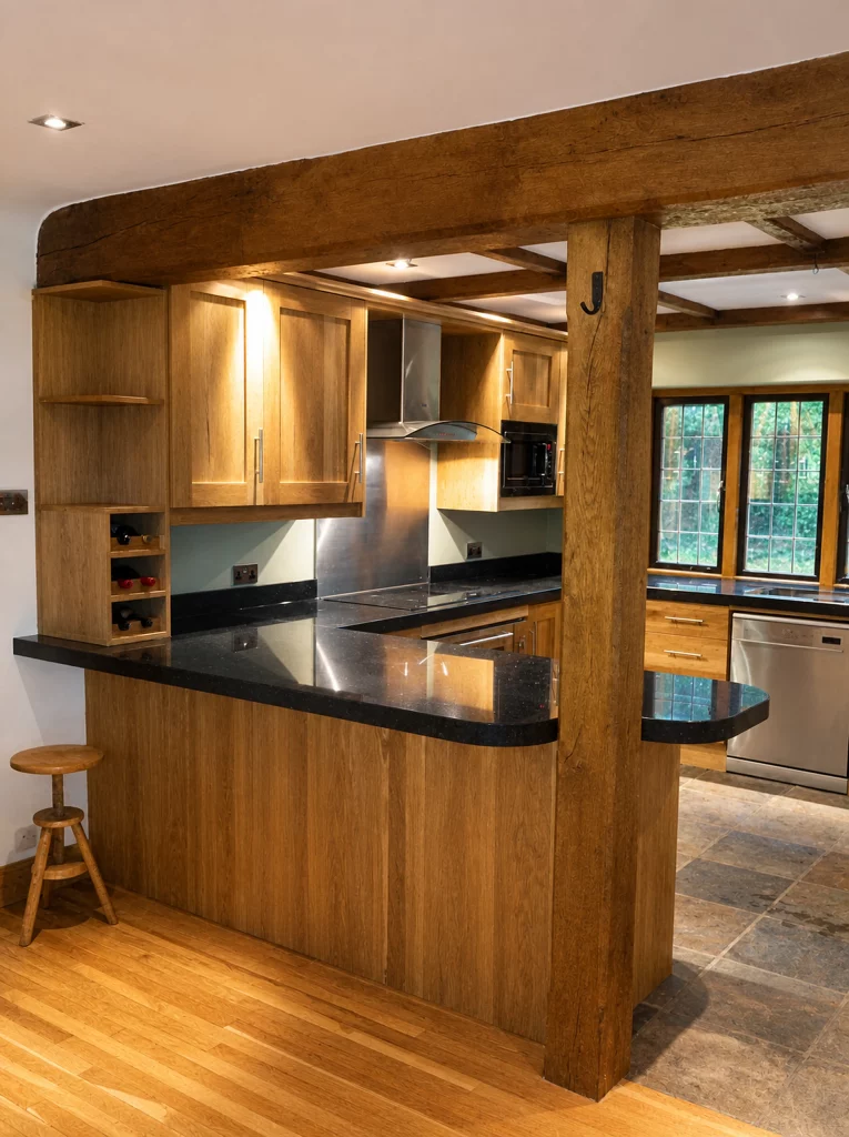 Handcrafted solid oak kitchen with dark stone worktops in a beamed interior, peninsula viewed from the adjoining room.