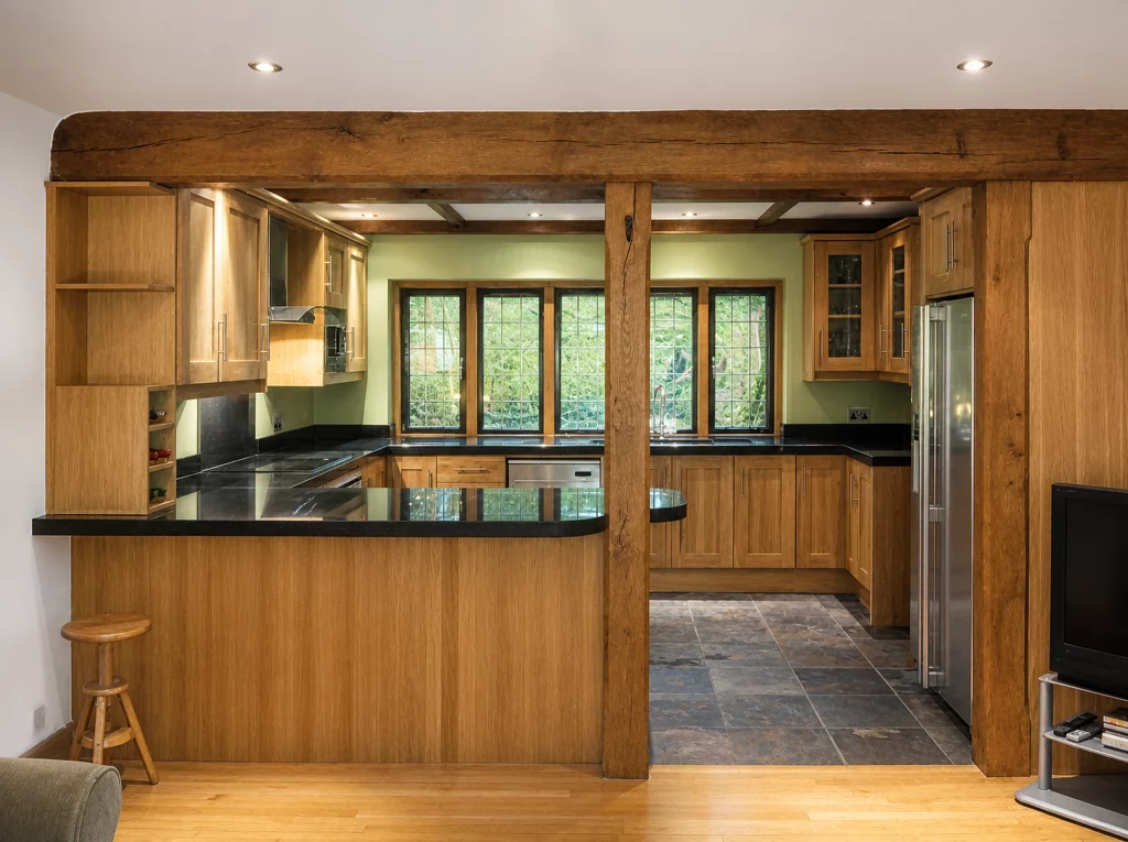 Handcrafted solid oak kitchen with dark stone worktops in a beamed interior, wide view through the oak frame into the kitchen.