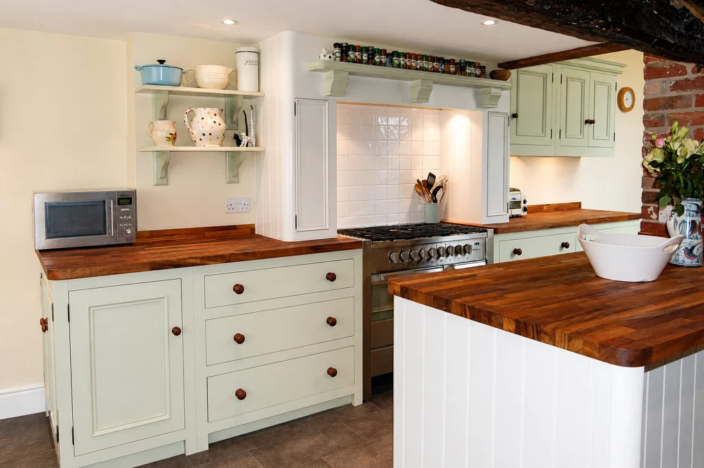 Painted country kitchen with replacement solid iroko worktops in Little Dunmow, range-cooker wall and peninsula with new iroko surfaces.