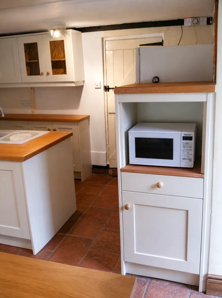 Compact painted Shaker kitchen with solid oak worktops in Little Waltham, tall appliance cabinet with a microwave shelf.