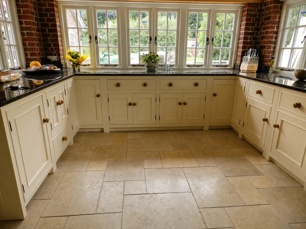Painted country Shaker kitchen with dark stone worktops and a range-cooker surround, wide view of the U-shaped cabinetry beneath the windows.