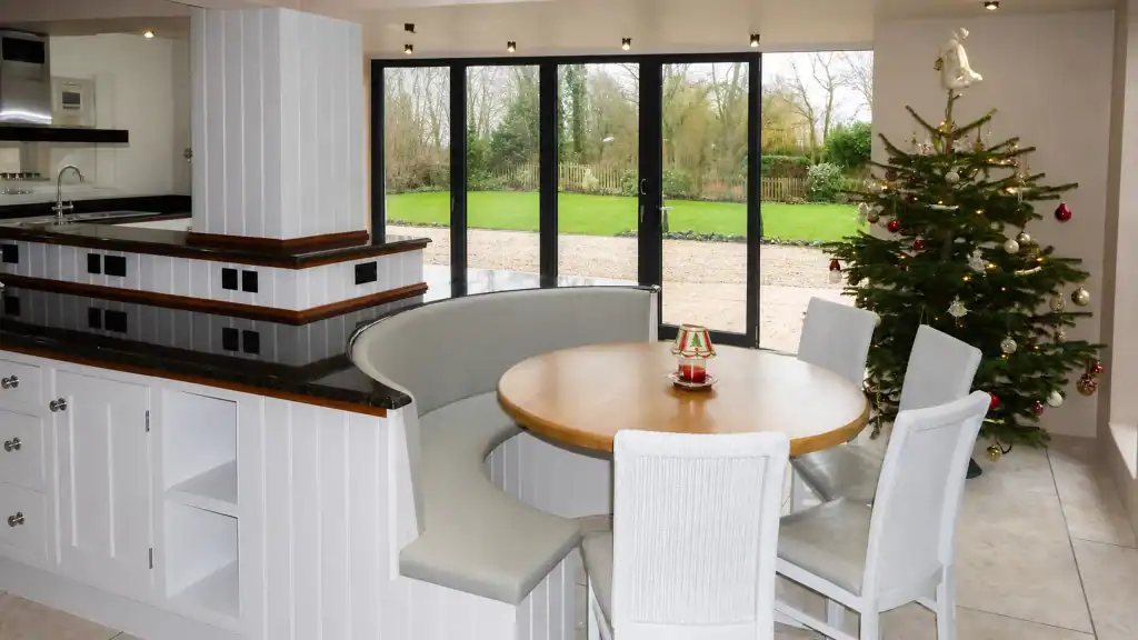 Painted pale-blue Shaker kitchen with dark granite worktops and oak details, dining nook opening onto the garden.