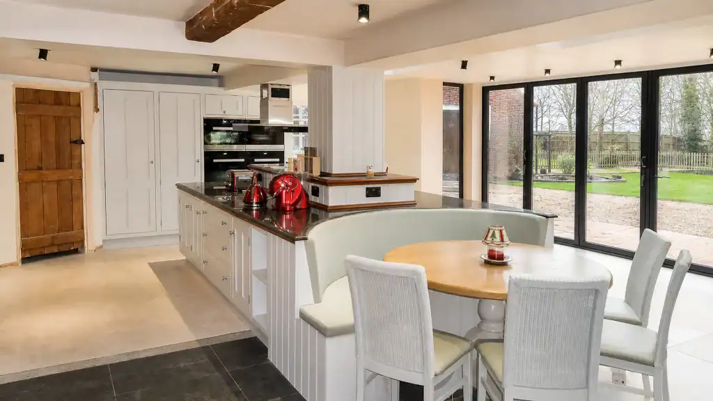 Painted pale-blue Shaker kitchen with dark granite worktops and oak details, wide room view showing peninsula, dining area and oak doors.