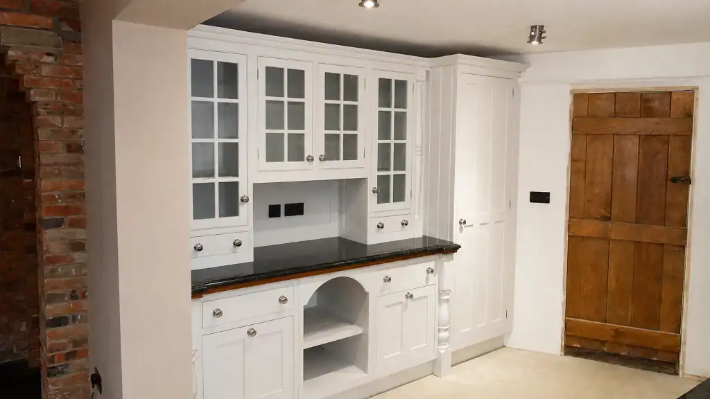 Painted pale-blue Shaker kitchen with dark granite worktops and oak details, painted dresser with glazed cupboards and open central display.