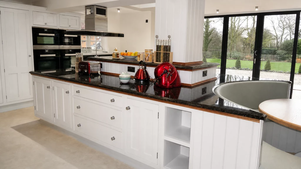 Painted pale-blue Shaker kitchen with dark granite worktops and oak details, long peninsula elevation with drawers and decorative oak inlays.