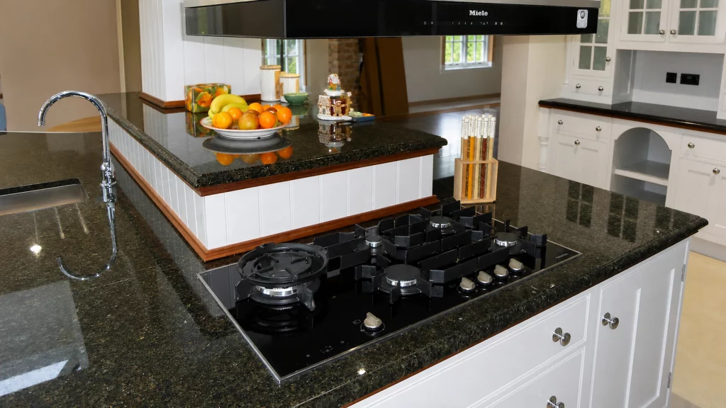 Painted pale-blue Shaker kitchen with dark granite worktops and oak details, granite-topped cooking peninsula with inset hob and overhead extractor.