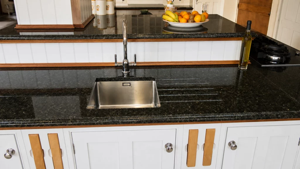 Painted pale-blue Shaker kitchen with dark granite worktops and oak details, undermounted stainless-steel sink in the granite peninsula.