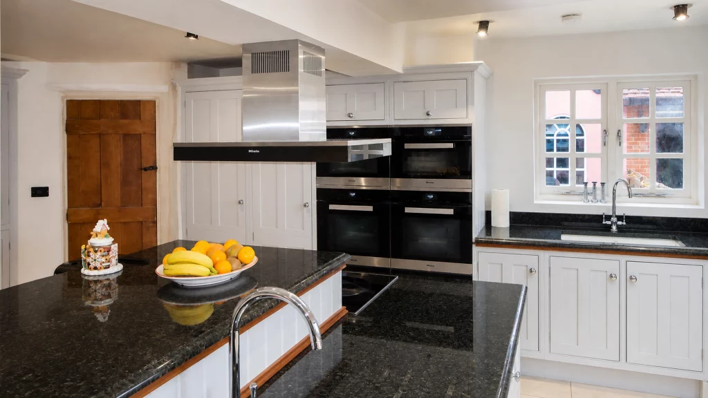 Painted pale-blue Shaker kitchen with dark granite worktops and oak details, kitchen overview from the sink towards the oven bank.
