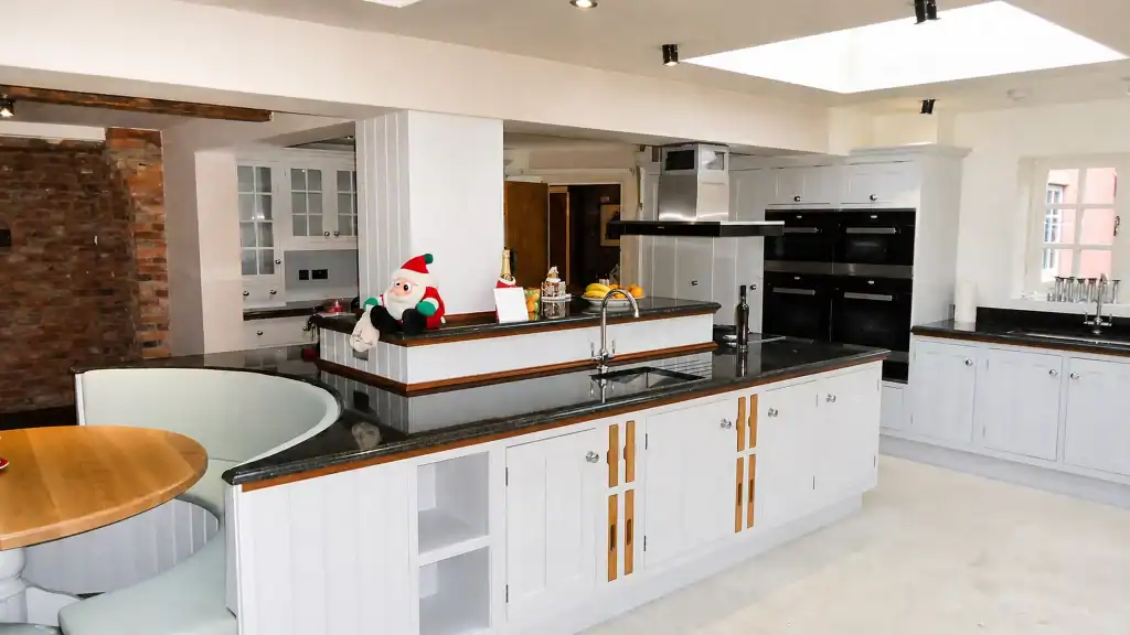 Painted pale-blue Shaker kitchen with dark granite worktops and oak details, wide view across the peninsula towards the integrated oven bank.