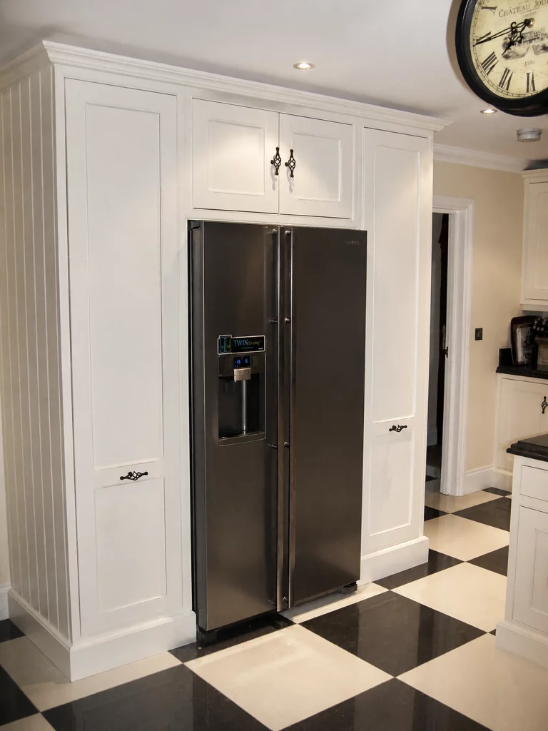 White painted Shaker kitchen with Star Galaxy granite and a central island in Wickham Bishops, tall painted housing around the American-style fridge-freezer.