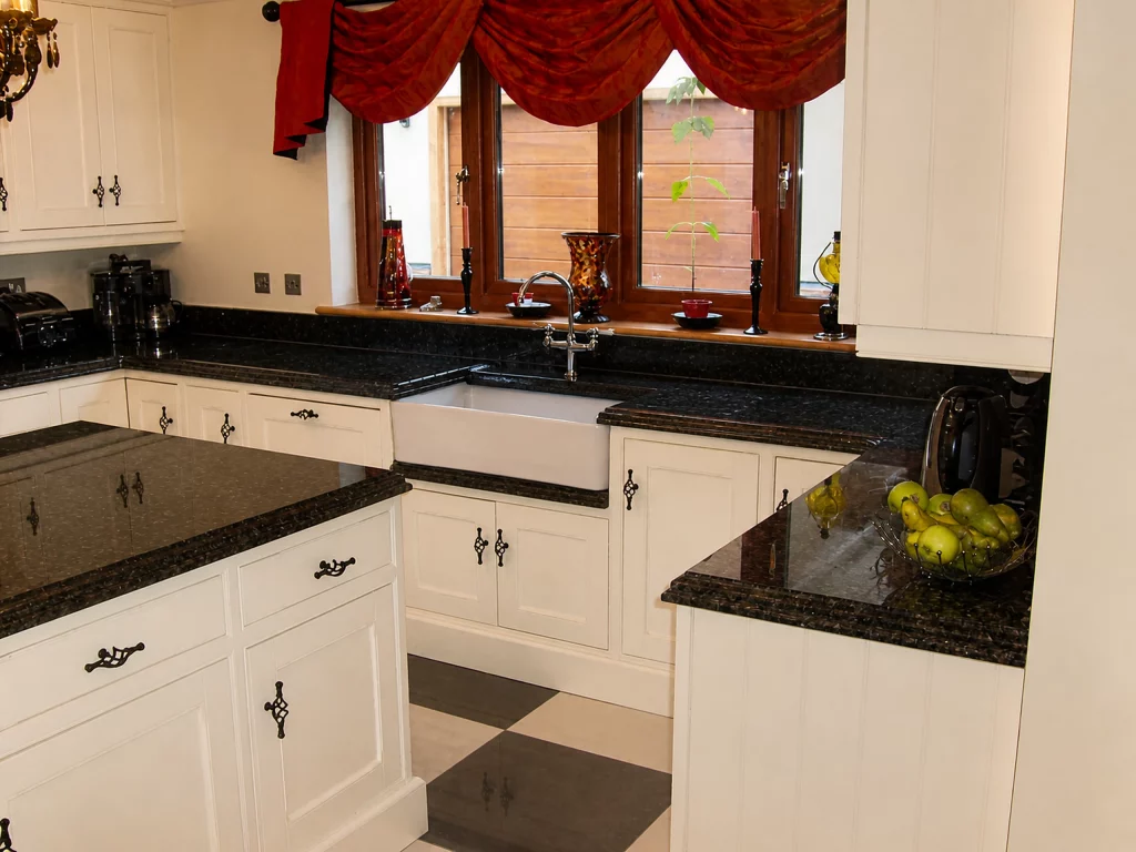 White painted Shaker kitchen with Star Galaxy granite and a central island in Wickham Bishops, sink run beneath the window with black granite worktop.